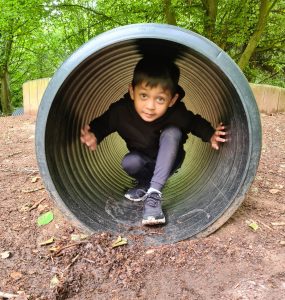 Child playing inside a large outdoor tunnel at Inchmarlo, a scenic residential area with natural surroundings.