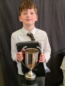Young boy in formal school uniform holding a trophy.