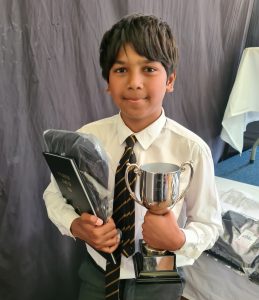 Young boy in school uniform holding trophy and certificate at Inchmarlo.