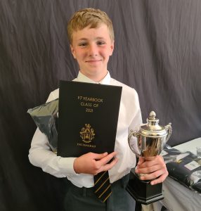 Young student holding diploma and trophy at Inchmarlo school celebration.