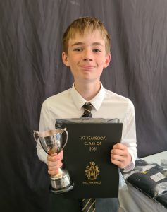 Young student holding a trophy and class certificate at Inchmarlo School graduation.