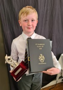 Young boy holding a graduation trophy and certificate, celebrating academic achievement at Inchmarlo School.