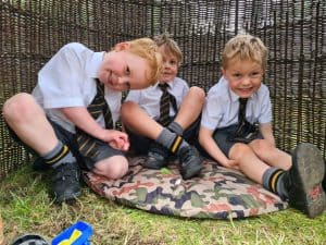 Three happy children sitting outdoors at Inchmarlo, enjoying a fun day in a scenic glamping setting.