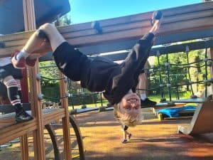 Young girl upside down on playground equipment with lush greenery background.