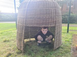 Child playing in woven outdoor play hut for kids.