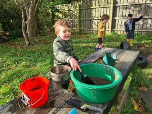 Children enjoying outdoor water play at Inchmarlo, surrounded by nature and a wooden fence.