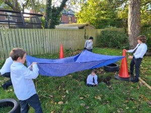Group of children playing with a blue parachute outdoors at Inchmarlo, a scenic park and outdoor activity area.
