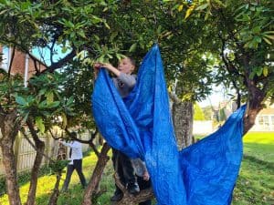 Child climbing a large blue fabric in a lush green park.