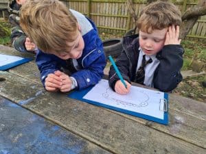 Two children drawing outside at Inchmarlo outdoor activity area.