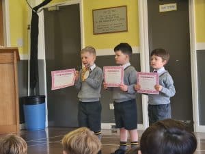 Three children holding certificates during school assembly at Inchmarlo.