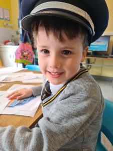 Young boy in school uniform wearing a cap, smiling at his desk in classroom.