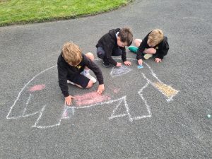 Three children drawing colorful chalk art on outdoor pavement.