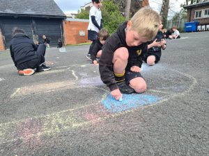 Children drawing with chalk on school playground for creative play.
