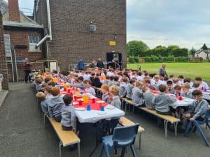 Outdoor school event at Inchmarlo with children seated at long tables, enjoying sunny weather.