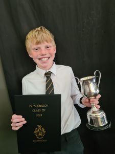Young student holding a trophy and yearbook, celebrating academic achievements.