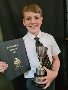 Smiling boy holding a trophy and a 2022 exam certificate, celebrating achievements at Inchmarlo.