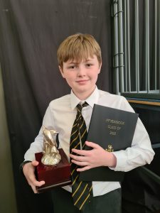 Young boy in school uniform holding an award and certificate, celebrating achievement at Inchmarlo.