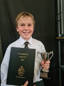 Young student holding a trophy and graduation book at Inchmarlo, celebrating academic achievement.