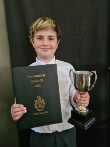 Young boy holding a Yearbook and trophy, celebrating academic achievement at Inchmarlo School.