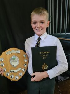 Young boy holding a school award and certificate smiling proudly.