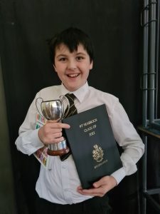 Young boy holding a trophy and a school certificate at Inchmarlo School, celebrating academic achievement.