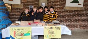 Students at Inchmarlo School standing behind a fundraising table outdoors.
