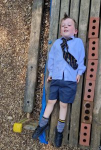 Young schoolboy in uniform leaning on a wall outdoors, representing Inchmarlo Academy’s community and education focus.