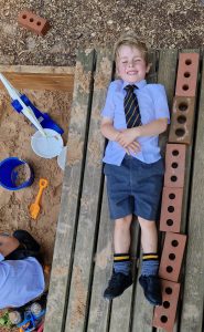 Young boy playing on outdoor wooden planks at Inchmarlo school with toys nearby.