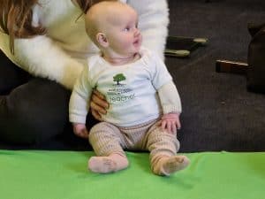 Adorable baby sitting on a green mat at Inchmarlo Nursery, Scotland's trusted childcare facility.