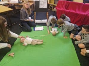 Children and instructor engaging in CPR training on a green mat at Inchmarlo preschool.