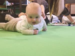 Adorable baby lying on green carpet at Inchmarlo care facility.