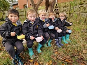 Children sitting outdoors in rain boots, enjoying nature at Inchmarlo.