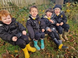 Four children sitting outdoors in rain gear at Inchmarlo outdoor play area.