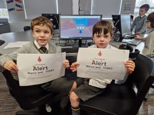Two children holding Alert signs in a computer room at Inchmarlo.