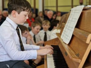 Young boy playing piano with audience watching in the background at Inchmarlo.
