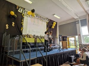 Students present on stage during school event. Celebration with decorations and audience engagement.