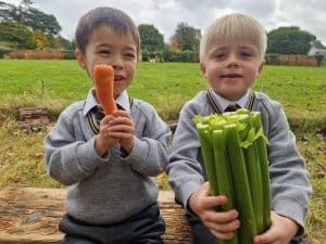Two children holding fresh vegetables and carrots outdoors at Inchmarlo.