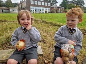 Two children enjoying outdoors at Inchmarlo, wearing school uniforms and holding snacks.