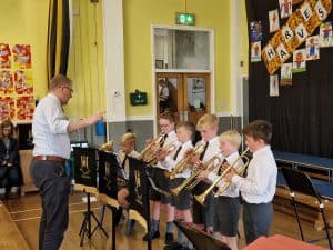 Young children playing brass instruments in school concert performance.