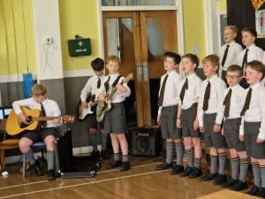 Primary school children singing and playing guitars at Inchmarlo school event.