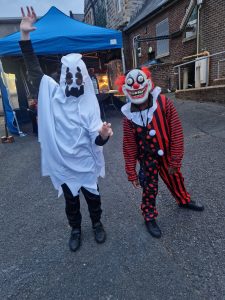 Two people in scary costumes at Inchmarlo Halloween event, wearing spooky masks and costumes.
