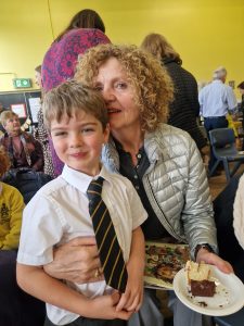 A smiling boy in school uniform with a woman at an indoor charity event.
