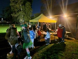 Outdoor gathering at Inchmarlo with people enjoying night-time festivities under a yellow tent.