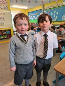 Two young boys in school uniforms standing in classroom.