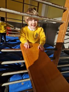 A cheerful girl in a yellow school uniform sliding at Inchmarlo playground.