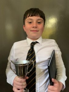Young boy in school uniform holding a trophy and tablet.