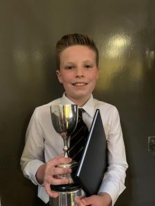 Young boy holding trophy and certificate at Inchmarlo event, celebrating success and achievement.