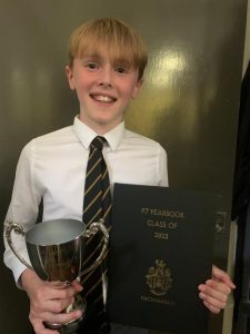 Boy in school uniform holding a trophy and certificate for academic achievement.