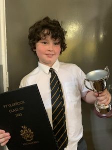 Young boy in school uniform holding trophy and certificate, celebrating achievement at Inchmarlo.