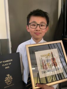 Young boy holding a framed award and book celebrating 2023 academic year.
